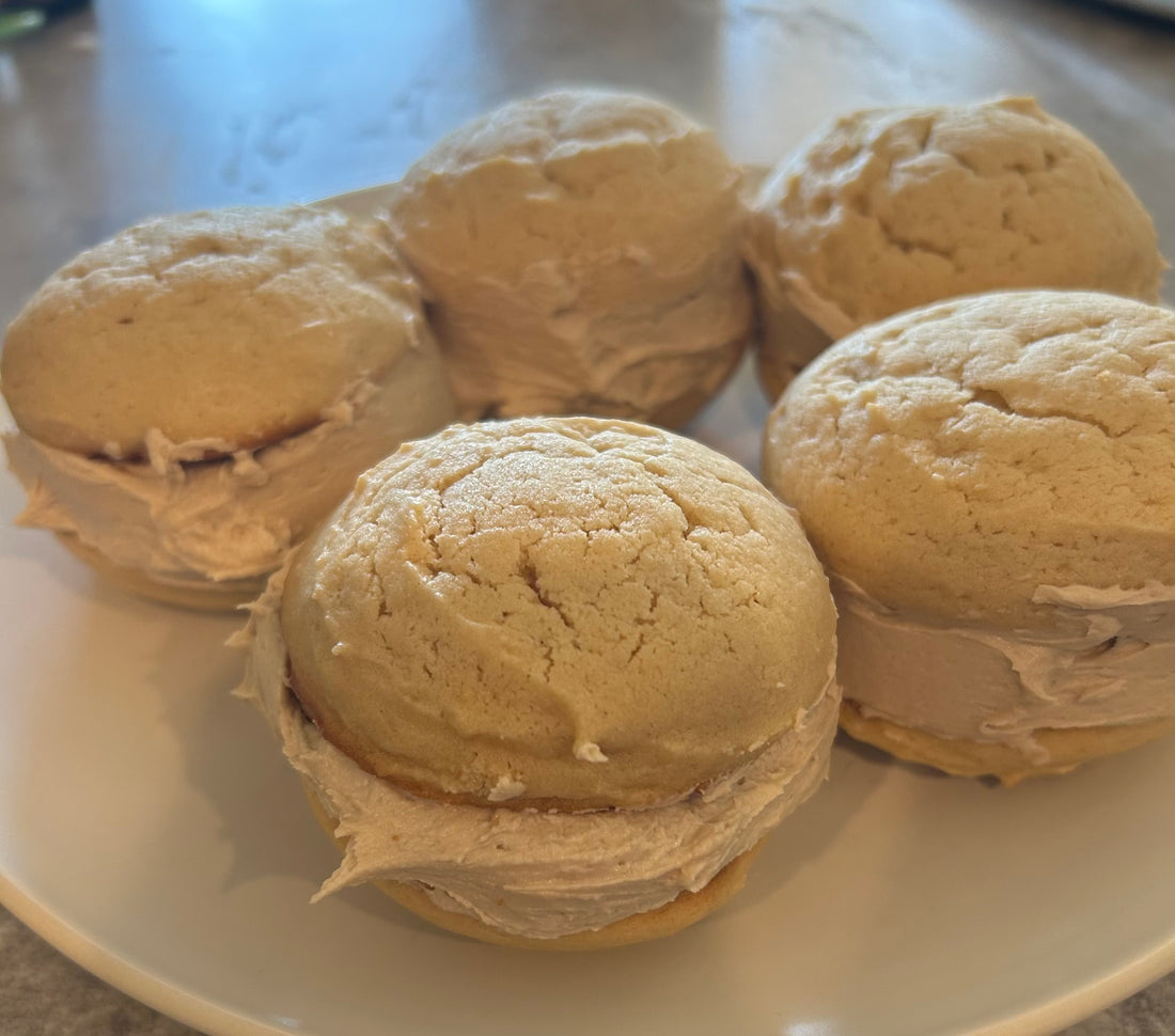 Five blond colored maple whoopie pies on a white plate filled with maple frosting.