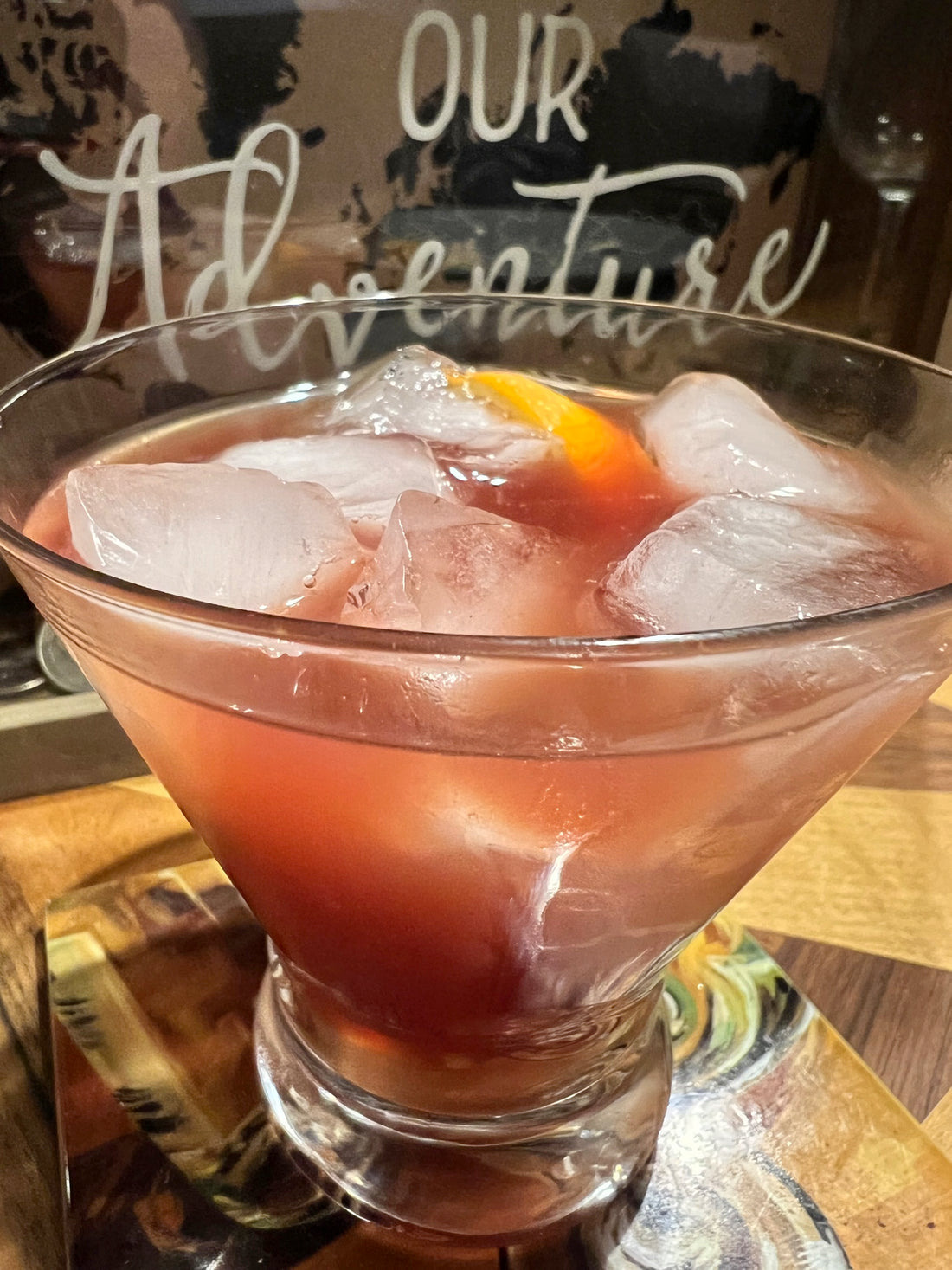 Wood's pink rum punch in a clear glass garnished with an orange slice with the words "Our Adventure" written in the background.