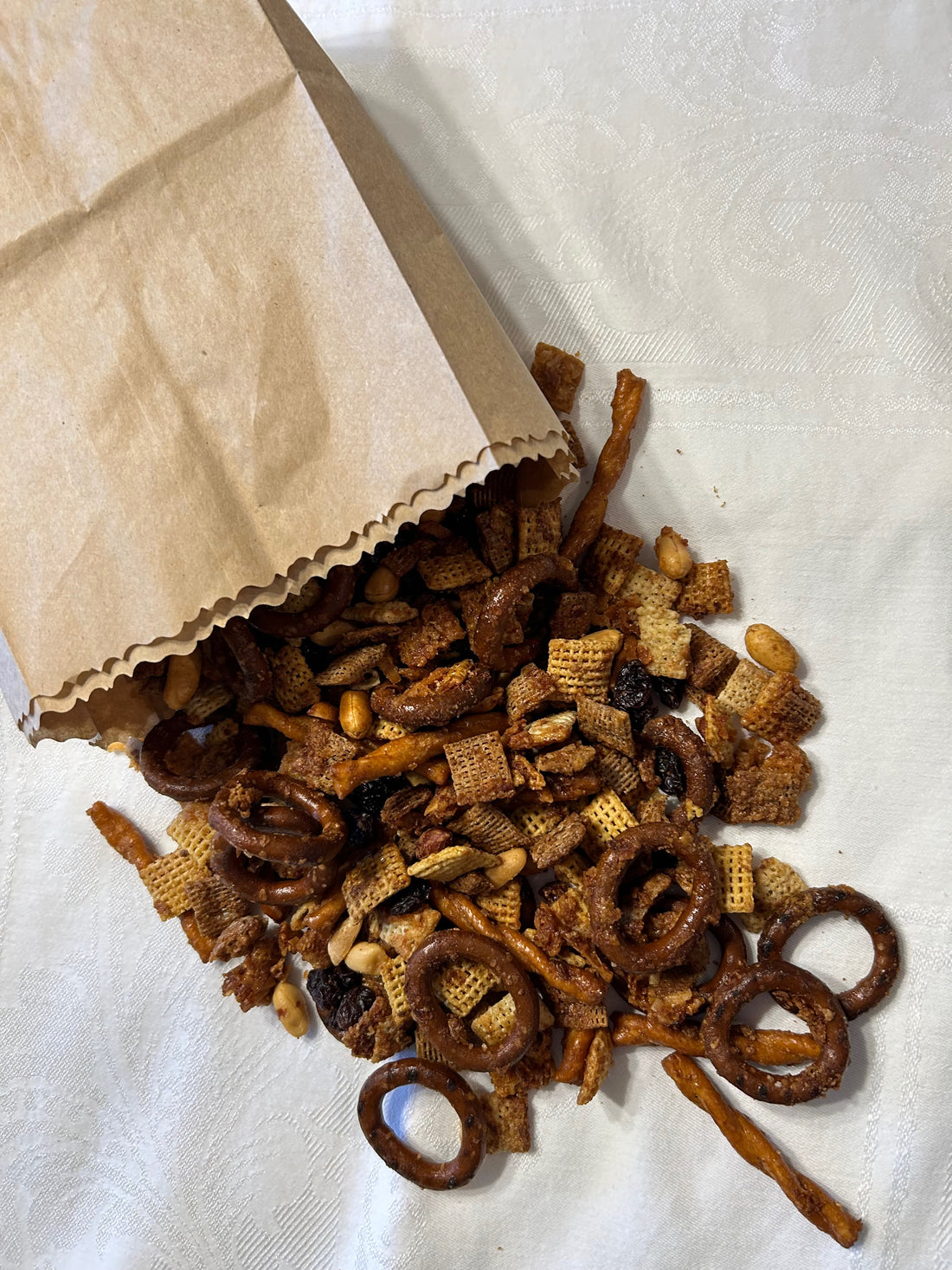 A paper bag filled with maple chex mix on a while table cloth.