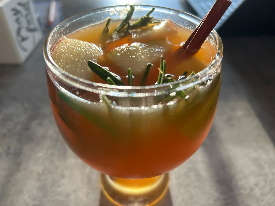 Wood's Holiday Punch in a clear glass with sprigs of rosemary and cinnamon in it.
