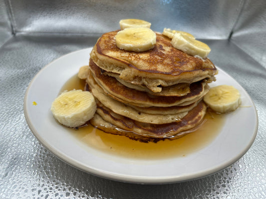 A stack of Peanut Butter Banana Pancakes topped with Maple Syrup and Banana.